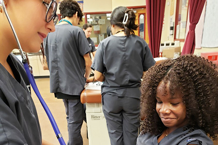 Student using a stethoscope on another student